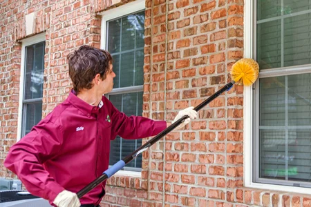 pest technician sweeping exterior of home