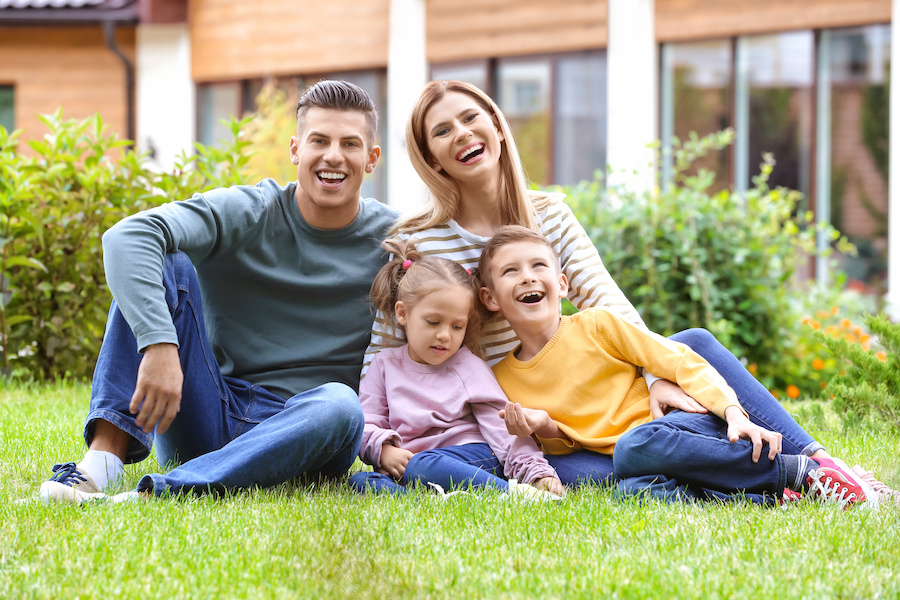 Happy family sitting on green grass in courtyard near their house